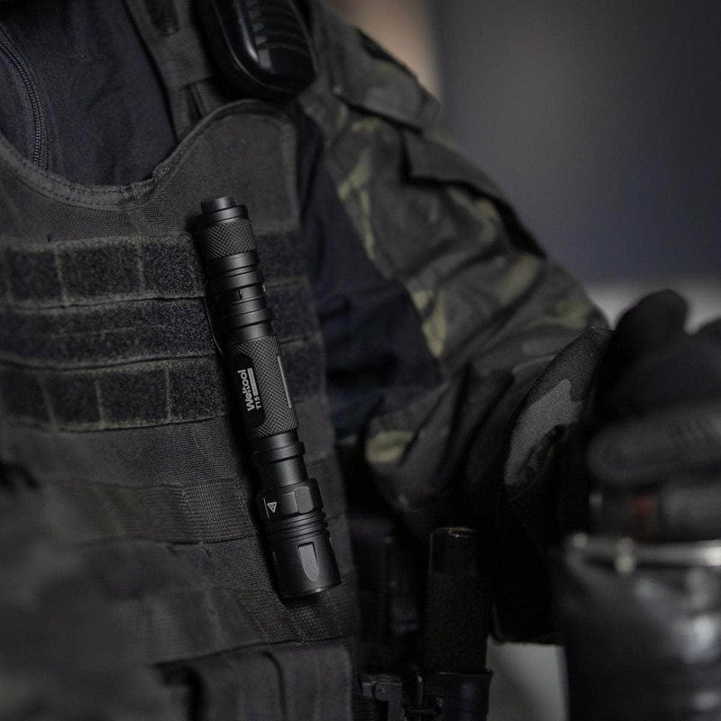 A Weltool T15 rechargeable LED tactical flashlight is clipped to the chest of a person dressed in dark camouflage body armor and tactical gear.
