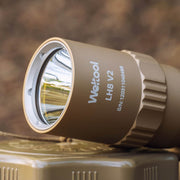 Close-up of a tan Weltool T16B V2 18350 LED flashlight showing the reflective lens and serial number printed on the side, placed on a textured tan surface.