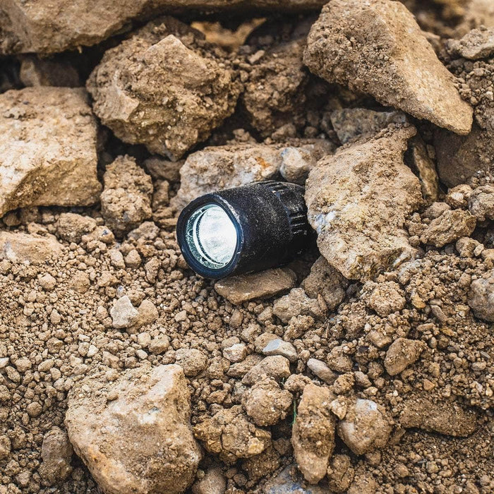 A durable Weltool T17 flashlight laying on top of a pile of rocks.