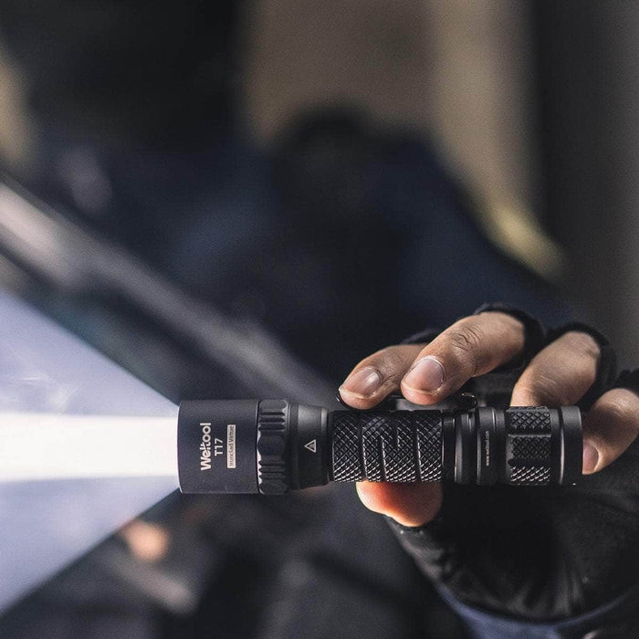 A person holding a Weltool T17 flashlight in front of a car.