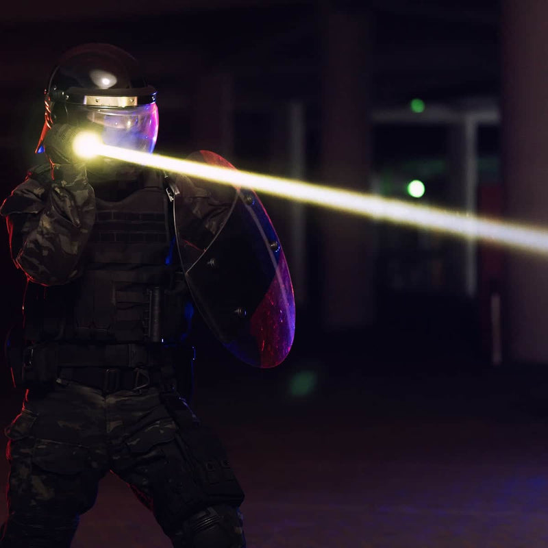A person in tactical gear and helmet holds a shield and aims a Weltool W15 “Flying Divinity” LEP Tactical Flashlight in a dark environment.