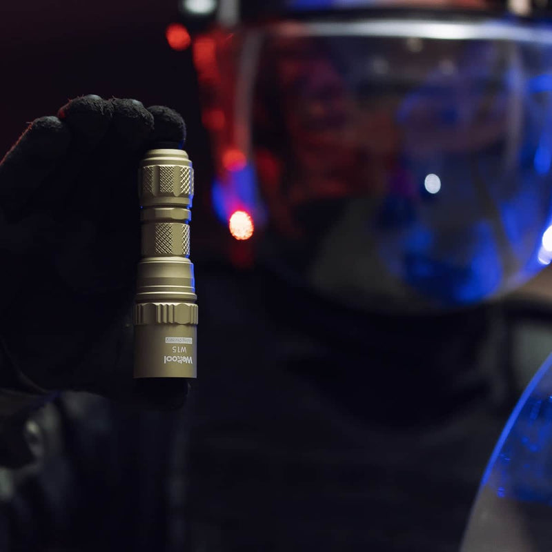 A person wearing gloves and a visor holds up the Weltool W15 “Flying Divinity” LEP Tactical Flashlight, blue and red lights reflecting on their face shield.