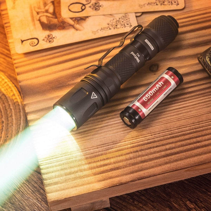 A Weltool W2 flashlight, the mini LEP tactical flashlight capable of illuminating up to 800 meters, is placed on a wooden table alongside a battery.