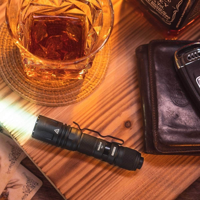 A Weltool W2 mini LEP tactical flashlight and a bottle of whiskey on a wooden table.