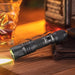 A Weltool W2 tactical flashlight on a table next to a bottle of whiskey.