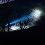 Using the Weltool W35B V2 Compact Weaponlight, a person walks along a dark, wooded path at night, illuminating the ground and surrounding brush.