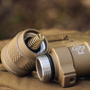 Close-up of two tan metal cylindrical parts from the Weltool W35B V2 Compact Weaponlight, with a visible coiled spring inside one piece, displayed on a brown textured surface.