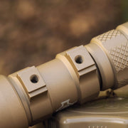 Close-up of a tan Weltool W35B V2 Compact Weaponlight mount with two threaded holes, textured grip, and machined details. Background is blurred.
