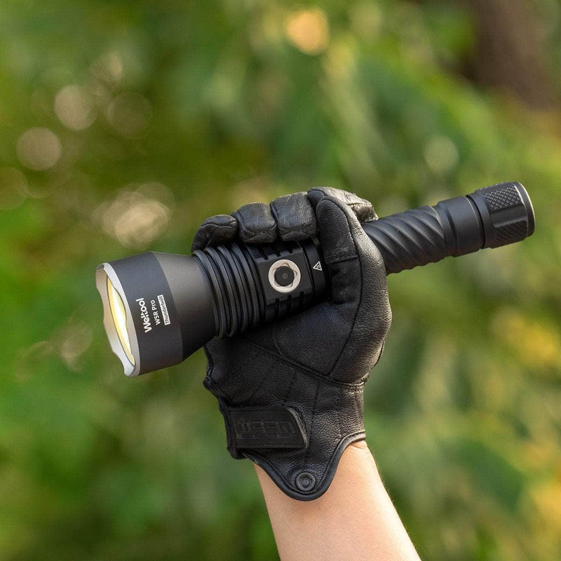 A gloved hand holds the Weltool W5R Pro LEP black long range flashlight outdoors against a blurred green background.