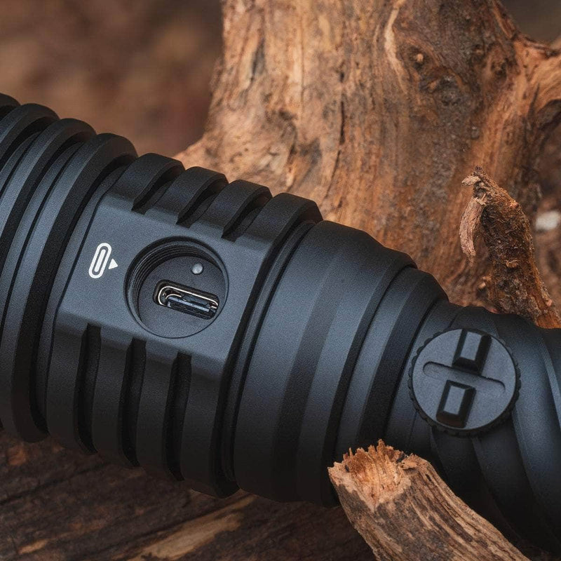 Close-up of the Weltool W5R Pro LEP, a black rechargeable flashlight featuring a USB charging port, resting against brown wood.