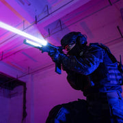 A tactical officer in dark gear aims a rifle equipped with the Weltool W65S, its intense beam cutting through the pink and blue-lit room.