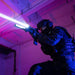 A tactical officer in dark gear aims a rifle equipped with the Weltool W65S, its intense beam cutting through the pink and blue-lit room.