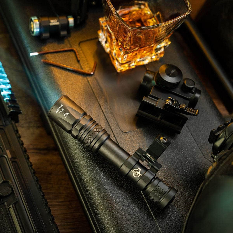 The Weltool W65S high candela flashlight and firearm accessories are displayed on a black hard case beside a glass of whiskey.