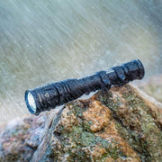 The Weltool W65S black long-range flashlight sits on a wet rock in the rain, showcasing its waterproof performance.