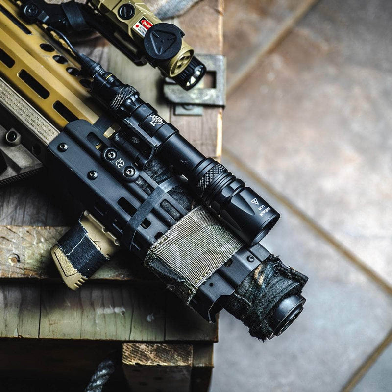 A close-up view of a tactical rifle with the Weltool W65S high candela flashlight, scope, and other accessories, resting on a wooden crate indoors.