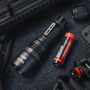 A black Weltool W7 LEP long-range tactical flashlight and a red 5000mAh 21700 lithium battery are on a textured dark surface, surrounded by gear. The flashlight delivers up to 700 lumens.