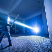 At night, a person stands on brick beneath a structure, holding the Weltool W7. Its 700-lumen LEP beam shines brightly toward them, casting dramatic shadows across the scene.