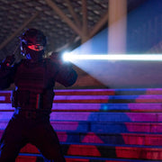 A person in tactical gear and helmet stands on steps at night, shining a Weltool W7 LEP tactical flashlight (700 lumens), with blue and red lights illuminating the scene.