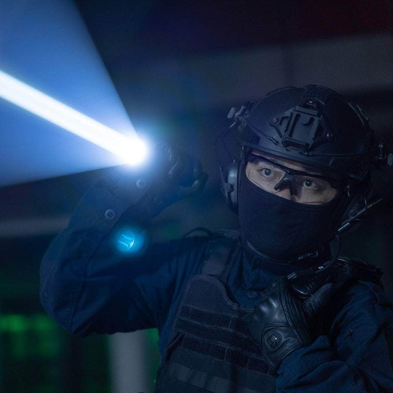 A person in tactical gear and helmet holds the Weltool W7, a 700-lumen LEP tactical flashlight, illuminating a long-range beam in a dark indoor setting.