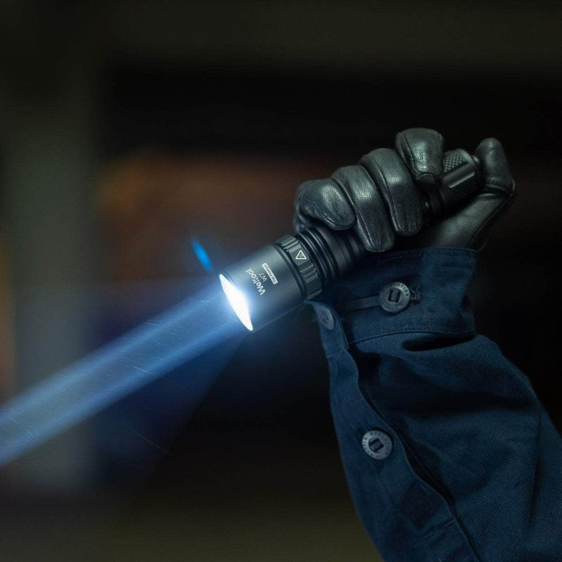 A person in black gloves and a blue jacket is holding the Weltool W7, a long-range LEP tactical flashlight that emits a bright 700-lumen beam in a dark environment.