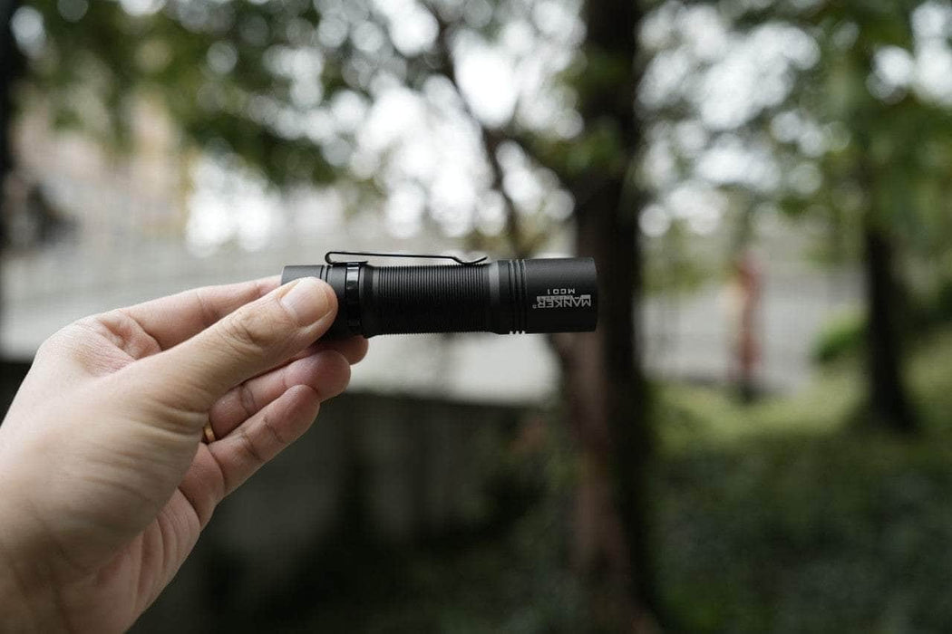 A person holding a Manker MC01 flashlight in front of a tree.