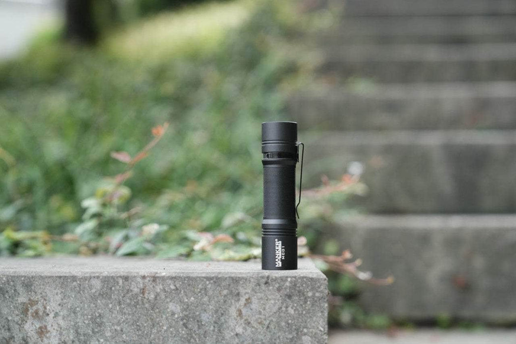 A Manker MC01 flashlight sits on a concrete step.
