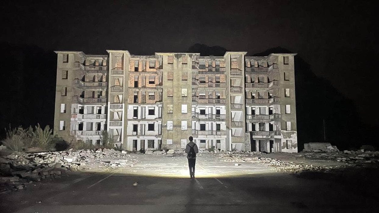 A person holding a Manker MK34 II standing in front of an abandoned building at night.