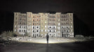 A person holding a Manker MK34 II standing in front of an abandoned building at night.