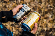A person holding a Manker MK34 II flashlight and a can of soda.