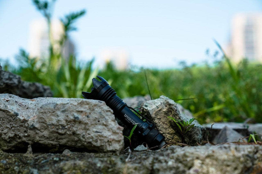 A Manker Striker - Aluminum flashlight laying on top of a rock in a grassy area.