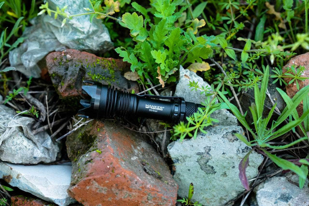 A Manker Striker - Aluminum flashlight laying on top of rocks in the grass.