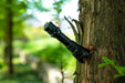 The Manker Striker - Aluminum is attached to a tree in the woods.