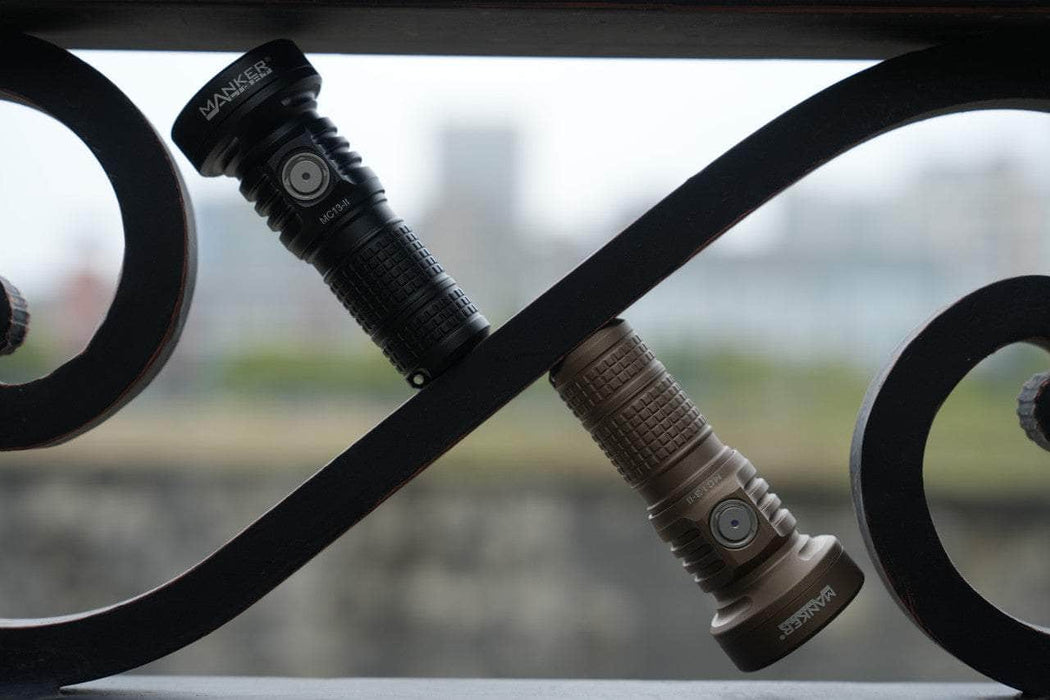 Two Manker MC13 II flashlights on a metal railing with a city in the background.