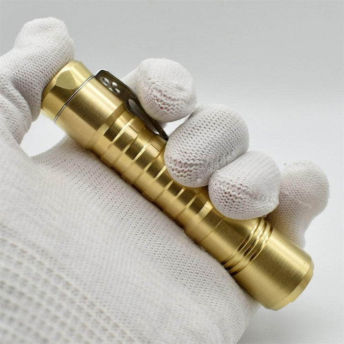 A person's hand holding a ReyLight Pineapple Brass flashlight.