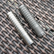 Two ReyLight Ti Dawn Triple flashlights, featuring Nichia 519A emitters and textured metal with clip attachments, sit side by side on a woven surface.