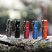 Four ReyLight x Vosteed Rook - Aluminum Triple Nichia 519a flashlights sitting on a tree stump.